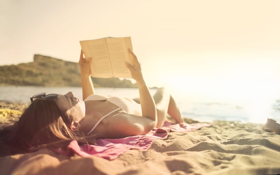 mulher lendo livro deitada numa toalha nas areias da praia