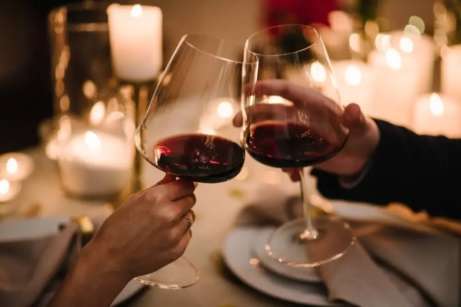 Saúde. Casal apaixonado bebendo vinho. Encontro romântico à luz de velas à noite. Mãos de homem e mulher segurando copos em casa. Brinde. Mesa de jantar arrumada para casal no dia dos namorados. Proposta de mão e coração.